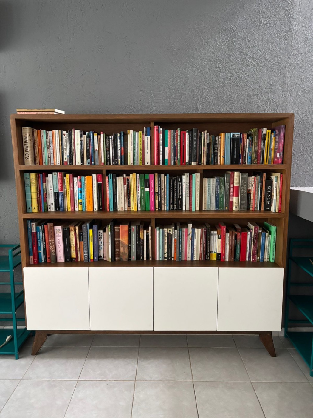 Librero de madera con repisas llenas de libros y puertas blancas abajo